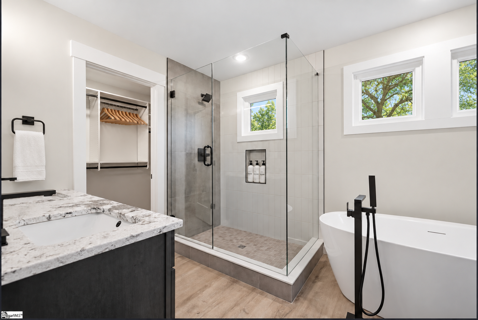 Bathroom with a glass shower, freestanding tub, and spring greenery visible through the windows